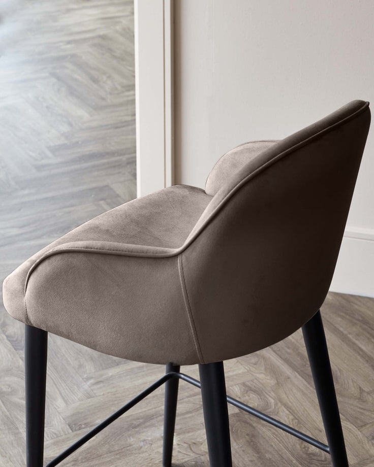 Lani bar stool in mocha velvet, shown from rear angle with black legs and footrest on herringbone wood floor.