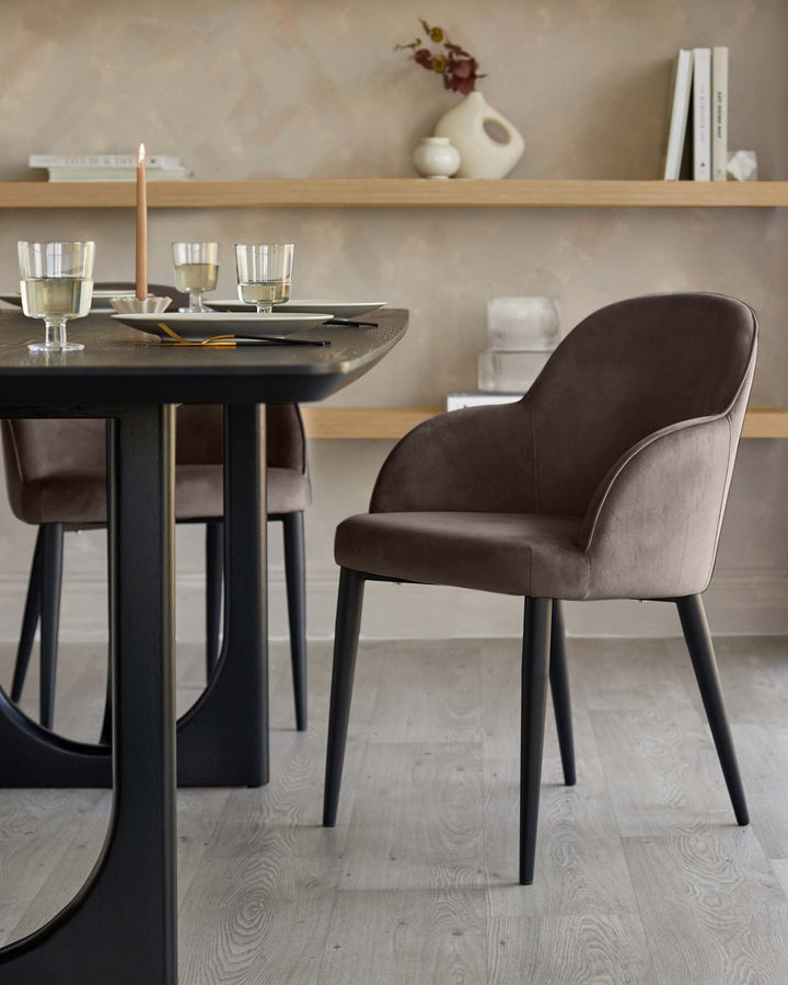 Mocha velvet dining chair with curved backrest and black legs, shown at round black table in dining room setting.