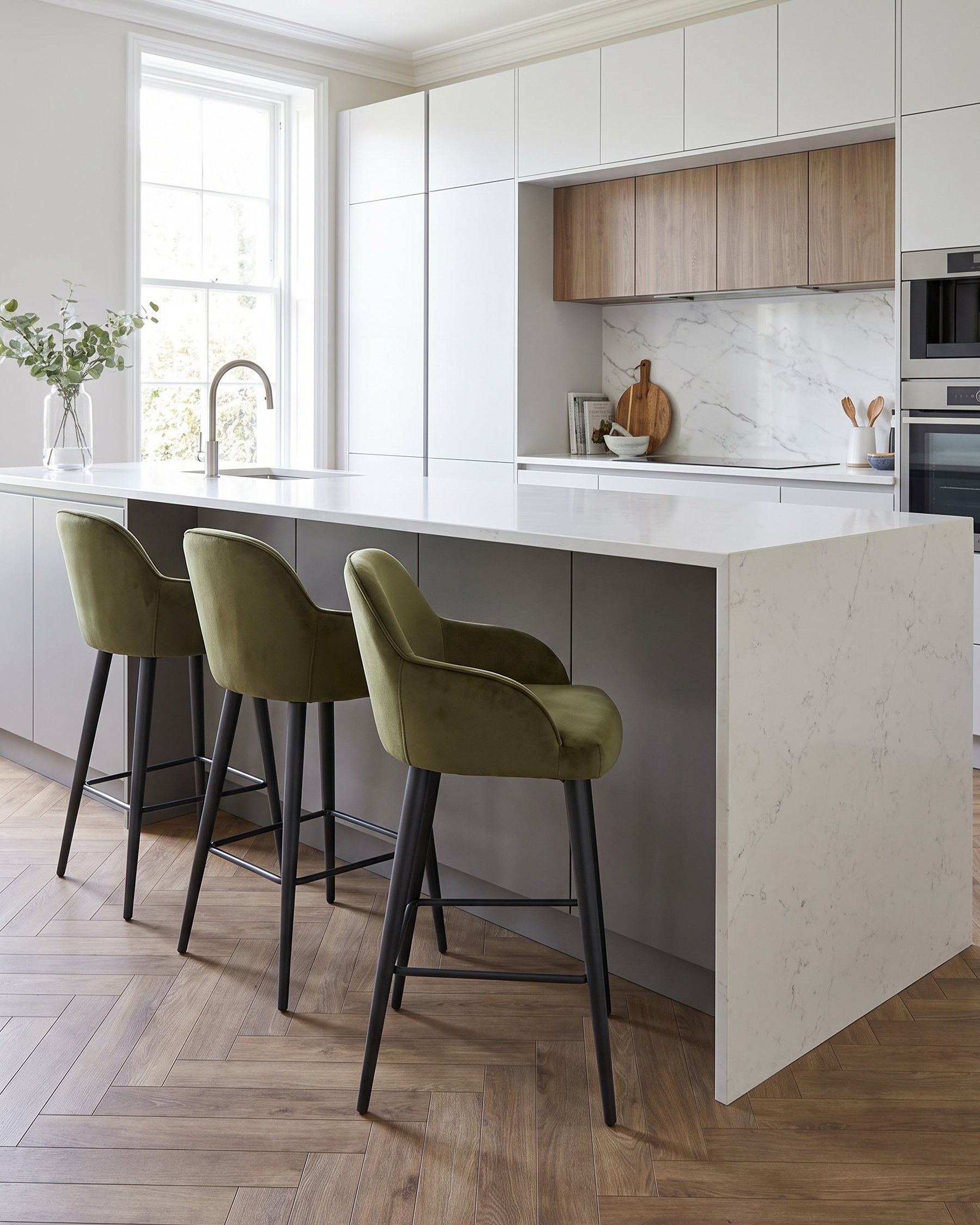 Lani bar stool in olive green velvet with black metal legs, shown at kitchen island with marble countertop.