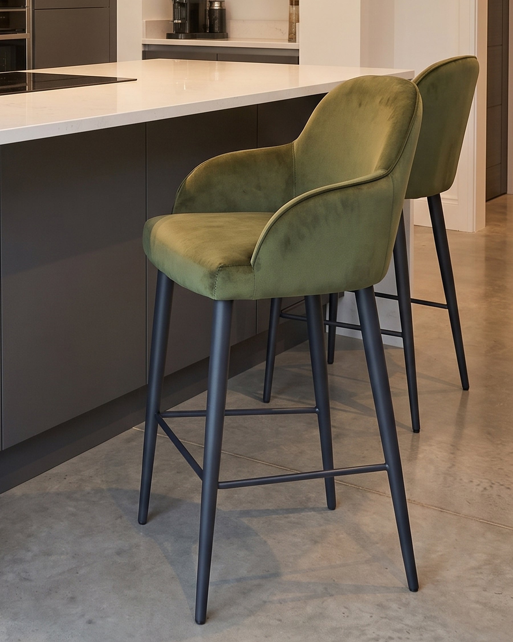 Lani bar stool in olive green velvet with black wooden legs, positioned at a kitchen island with white countertop.