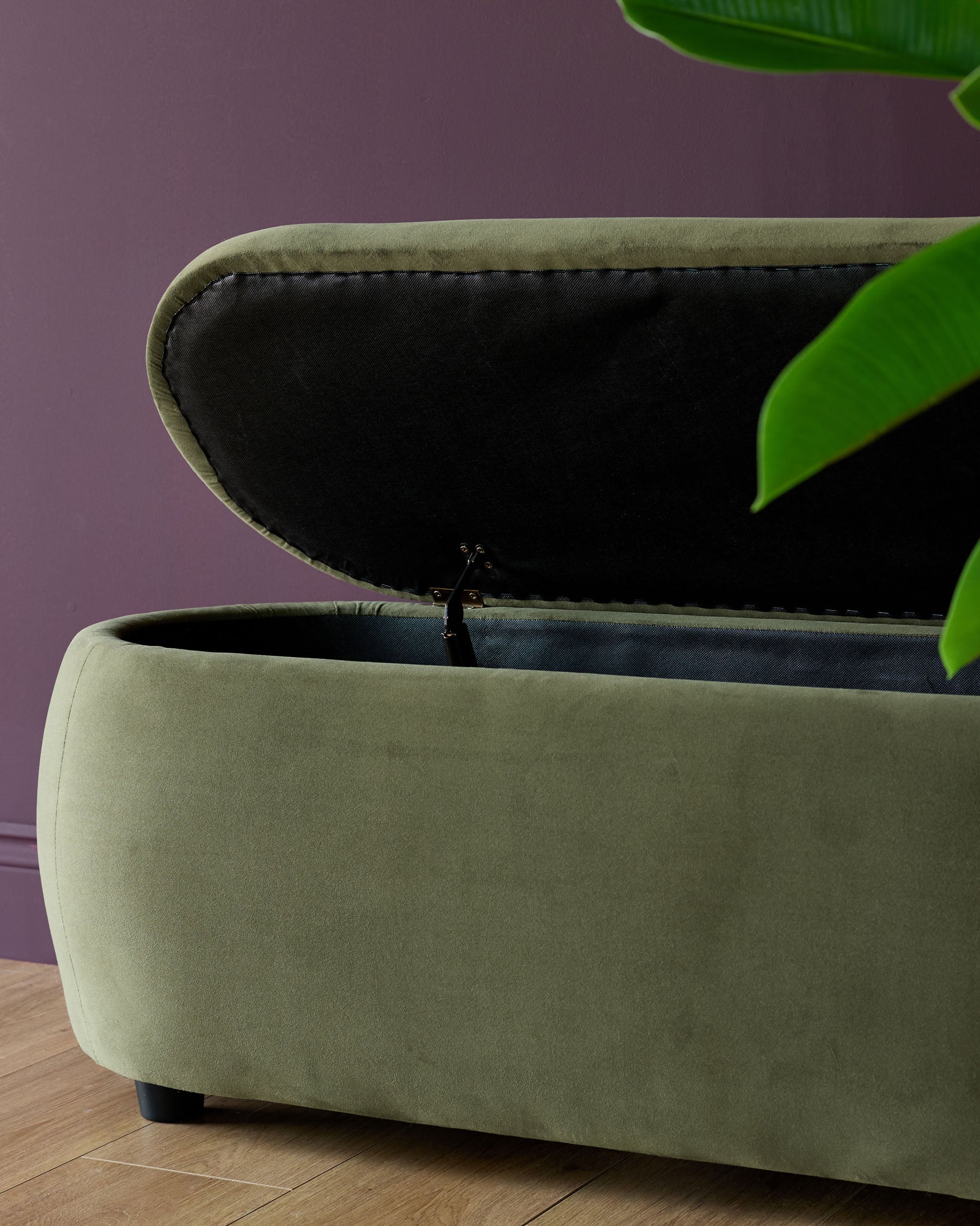 Olive green ottoman storage trunk with hinged lid, set against a purple wall, on wooden flooring.