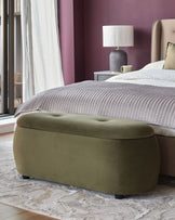 Bedroom with olive green ottoman at the end of a king-size bed, bedside lamp and textured rug.