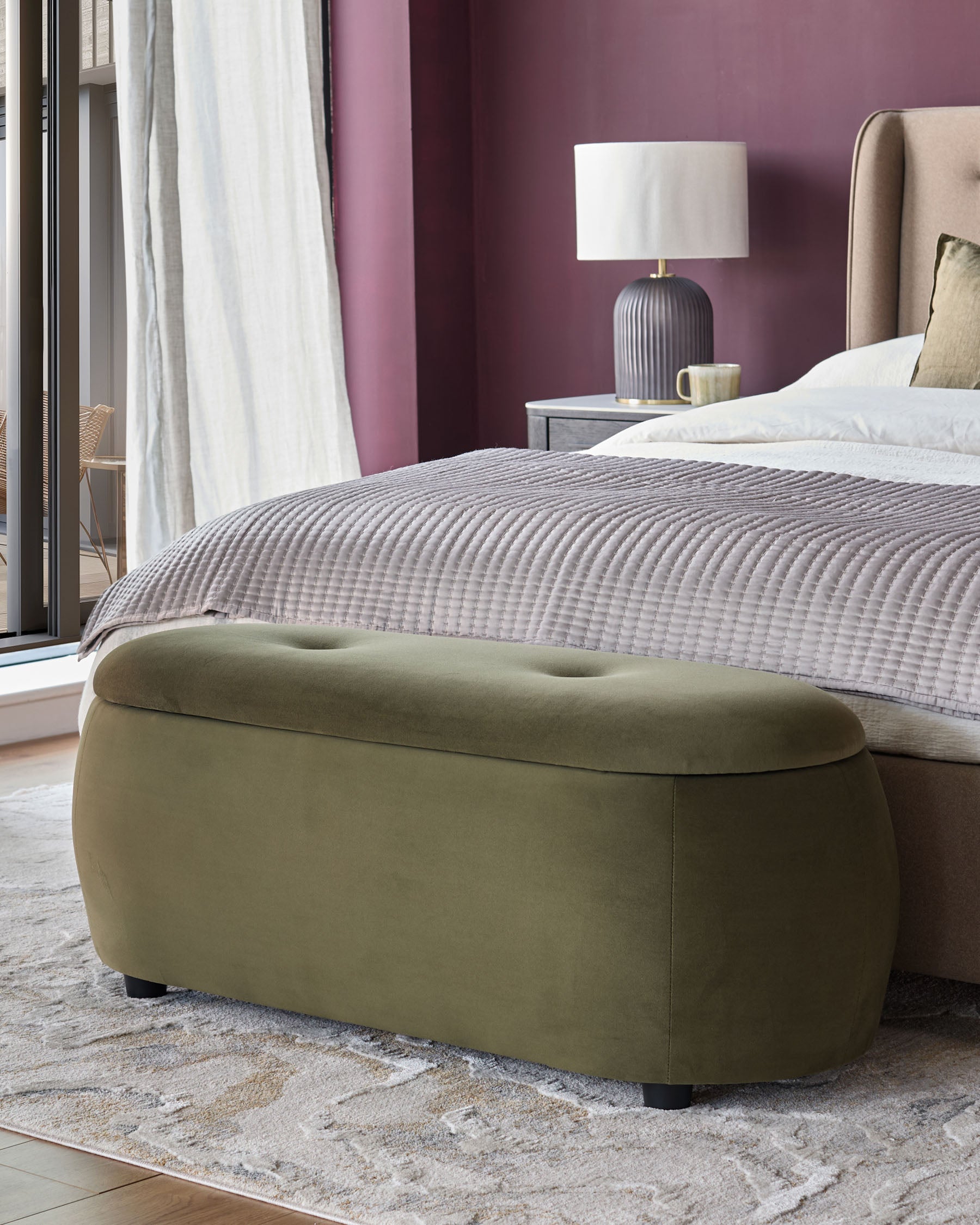 Bedroom with olive green ottoman at the end of a king-size bed, bedside lamp and textured rug.