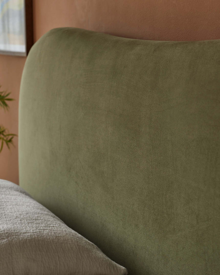 Close-up of an olive green velvet headboard and pillow, showcasing a bed frame from a furniture company.