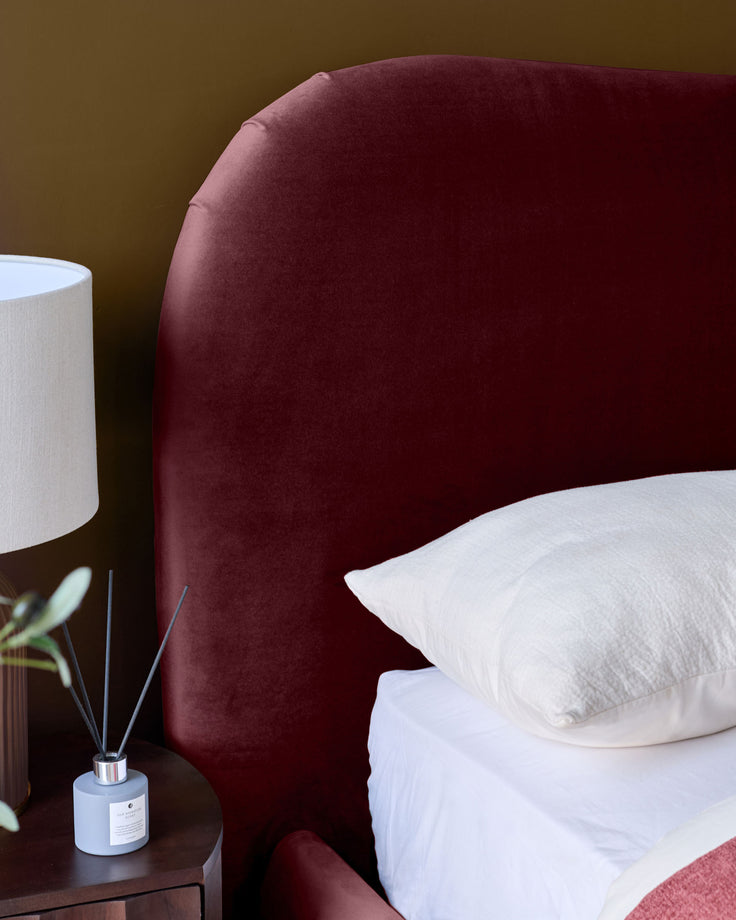 Lani king ottoman bed in plum velvet with rounded headboard, styled with white pillows and bedding.
