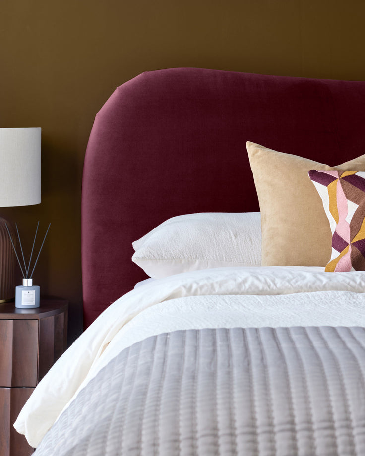 Lani King Ottoman Bed in plum velvet with curved headboard, white bedding, and decorative patterned pillow.