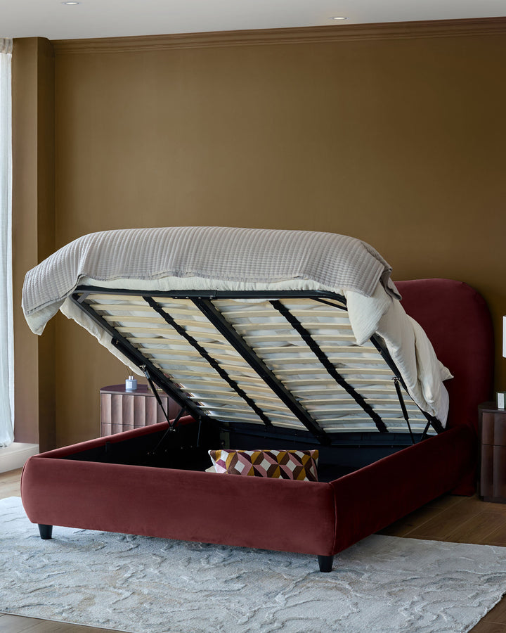 Plum velvet ottoman bed with open storage compartment, showing wooden slatted base and light striped mattress topper.