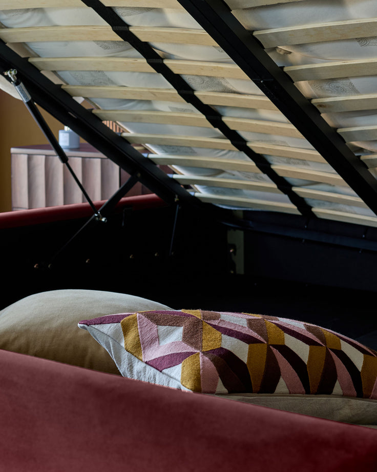 Plum velvet ottoman bed with open storage, geometric patterned cushion, natural wood slatted base visible from above.