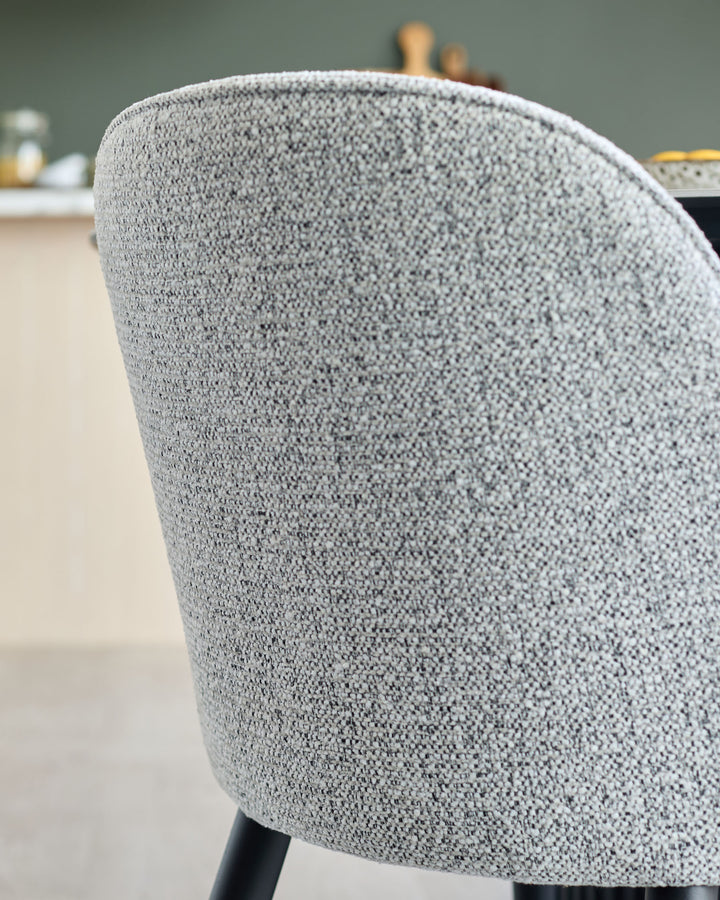 Close-up of a textured grey upholstered chair with black legs, adding modern style to any dining area.