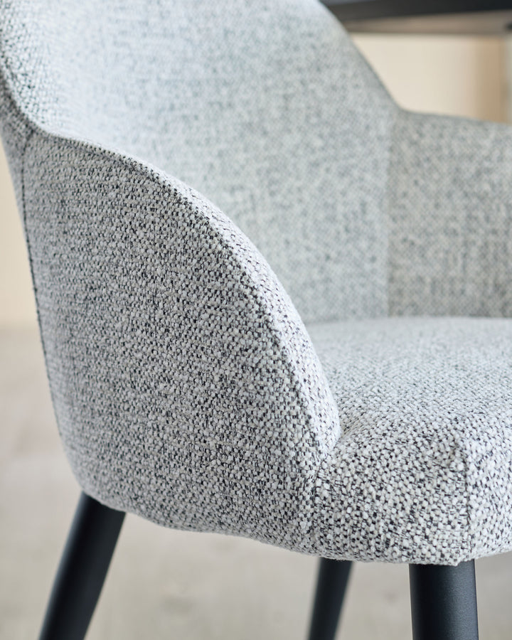 Close-up of a stylish grey upholstered chair with black legs, showcasing the fabric texture and modern design.