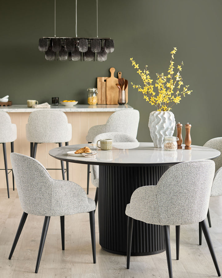 Dining area with round table and chairs, featuring bar stools in the background. Stylish and modern furniture.