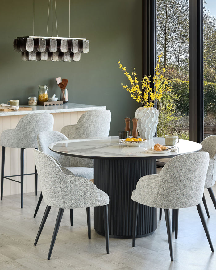 Dining set featuring a round marble-topped table with a fluted base, complemented by fabric-upholstered chairs and counter stools.