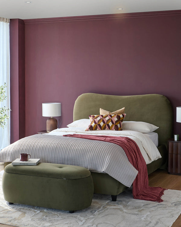 A stylish bedroom featuring an upholstered bed and ottoman in olive green, complemented by a plum wall and neutral rug.
