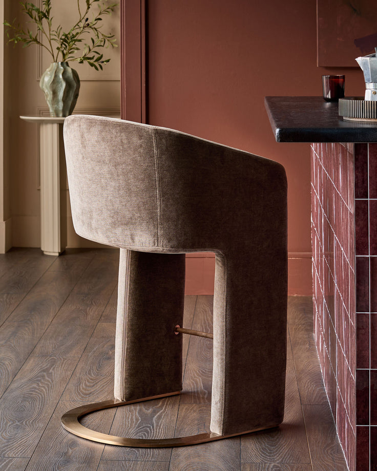 Leighton brushed bronze cantilever bar stool in mocha fabric, shown at angle displaying curved backrest and metal footrest.