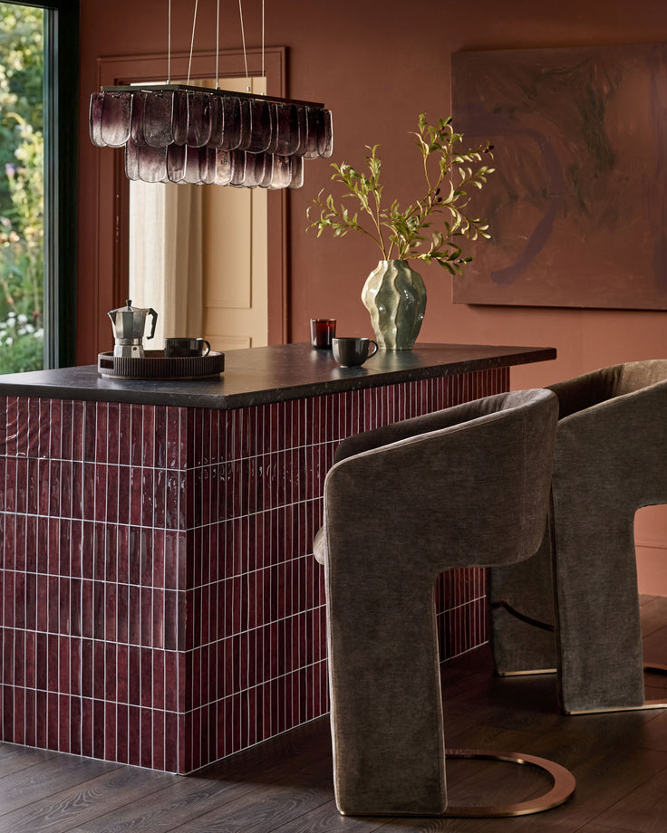 Leighton brushed bronze cantilever bar stool in mocha fabric, shown at dining counter in modern interior setting.