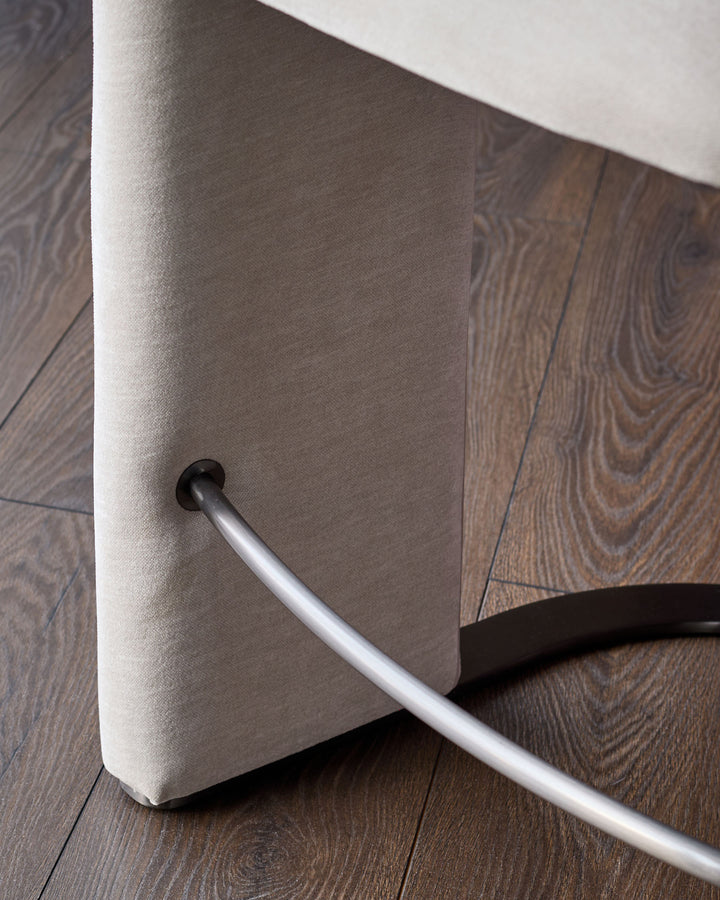 Leighton bar stool close-up showing natural grey fabric seat and polished steel cantilever base on wood flooring.
