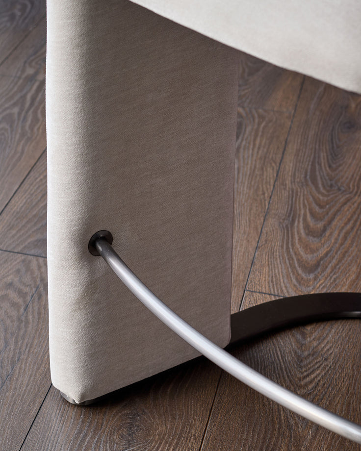 Leighton bar stool close-up showing natural grey fabric seat and polished steel cantilever base on wood flooring.