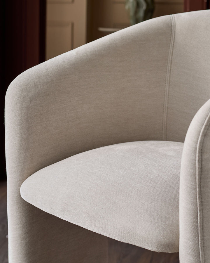 Cream fabric armchair with curved backrest and rounded seat, detailed close-up view showing textile weave and seam detailing.