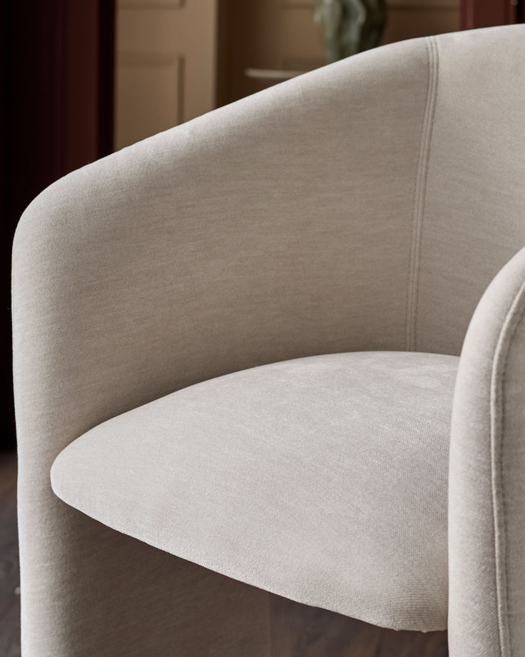 Cream fabric armchair with curved backrest and rounded seat, detailed close-up view showing textile weave and seam detailing.