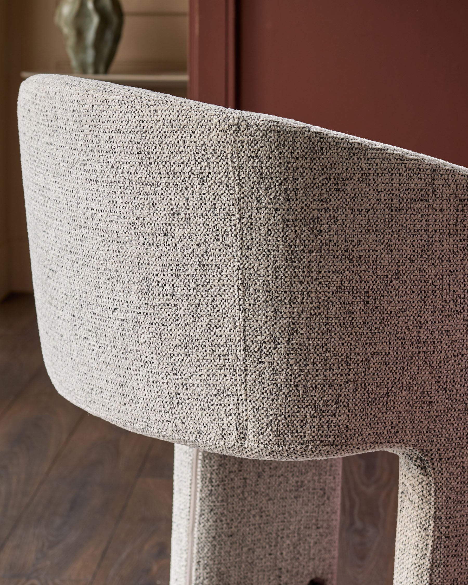 Grey fabric cantilever bar stool with curved backrest, shown from side angle detail.