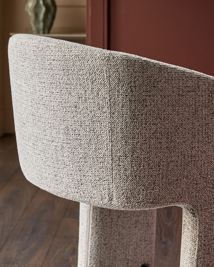 Grey fabric cantilever bar stool with curved backrest, shown from side angle detail.