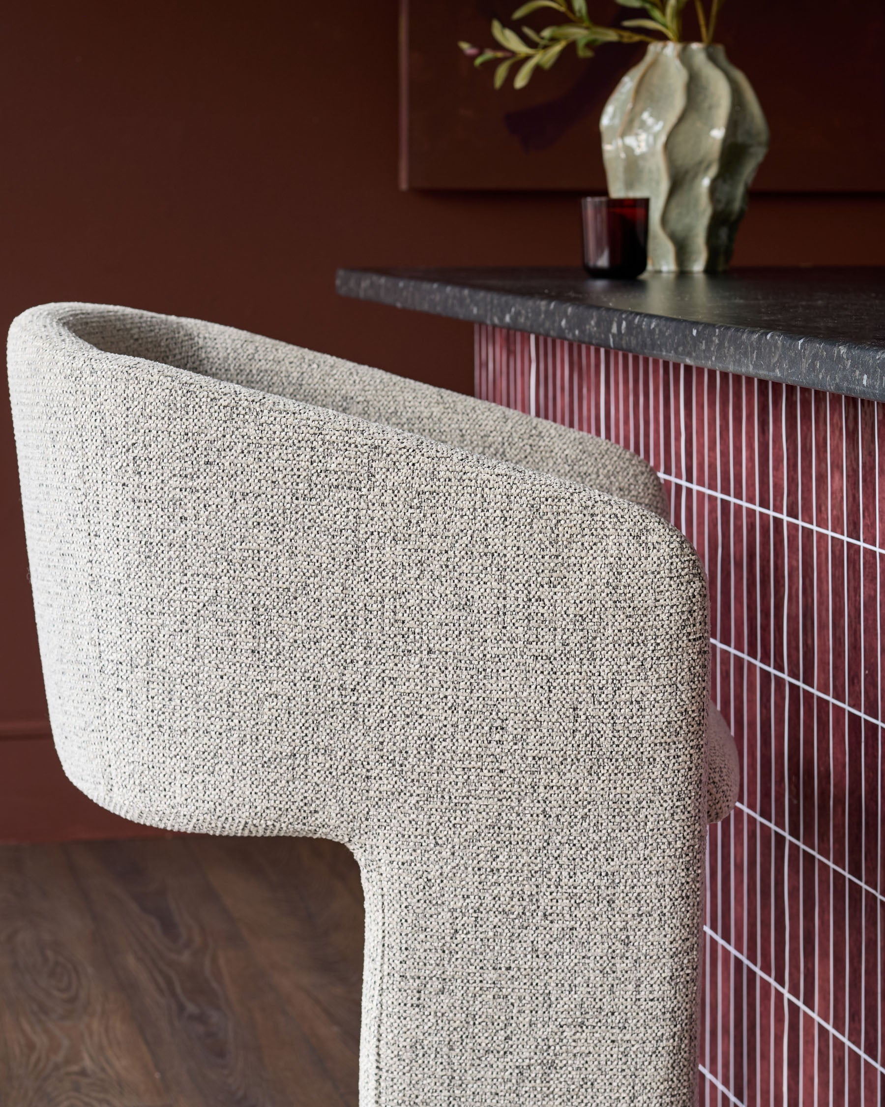 Leighton bar stool in grey fabric with curved backrest, shown beside black steel cantilever base in styled interior setting.