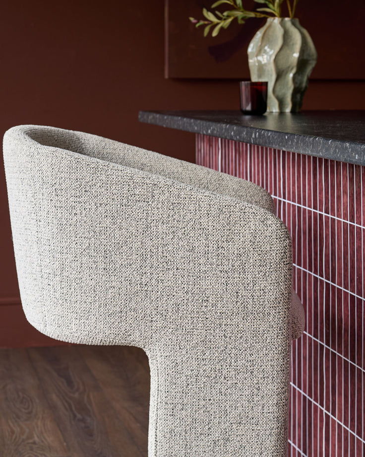 Leighton bar stool in grey fabric with curved backrest, shown beside black steel cantilever base in styled interior setting.
