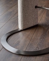 Leighton black steel cantilever bar stool with grey fabric seat, showing curved metal base and backrest detail on wood flooring.