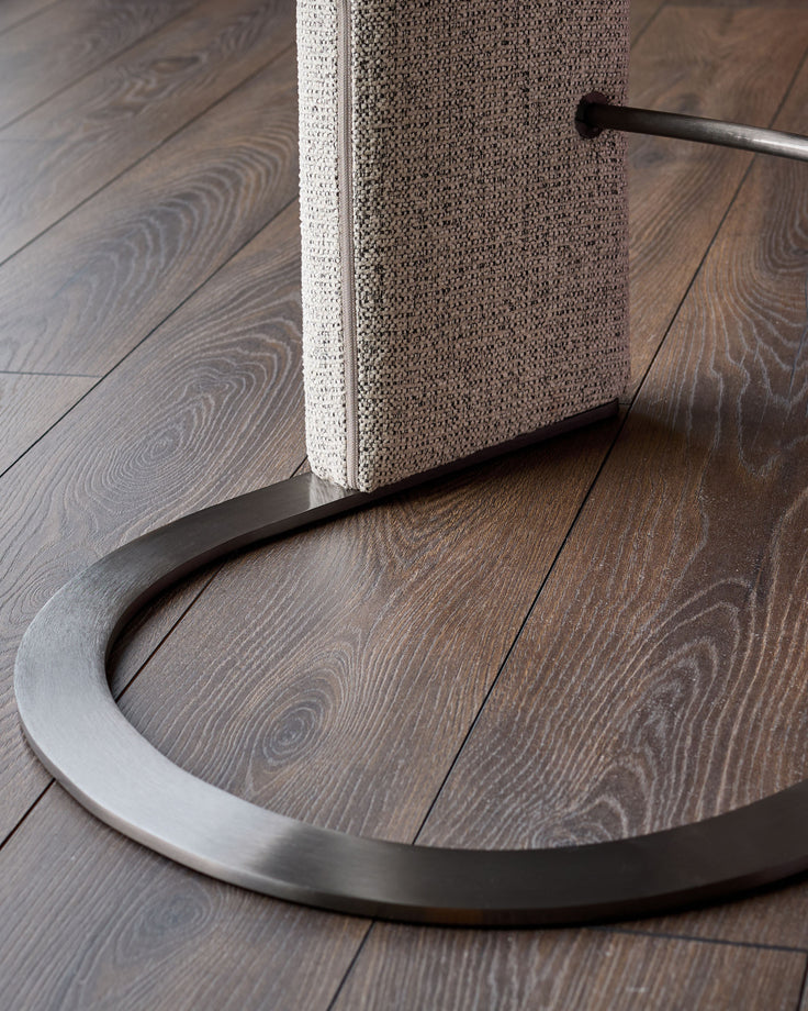 Leighton black steel cantilever bar stool with grey fabric seat, showing curved metal base and backrest detail on wood flooring.