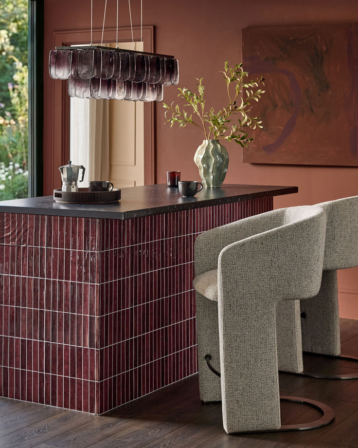 Leighton grey fabric cantilever bar stool with black steel frame, shown at modern dining counter in burgundy and cream interior.