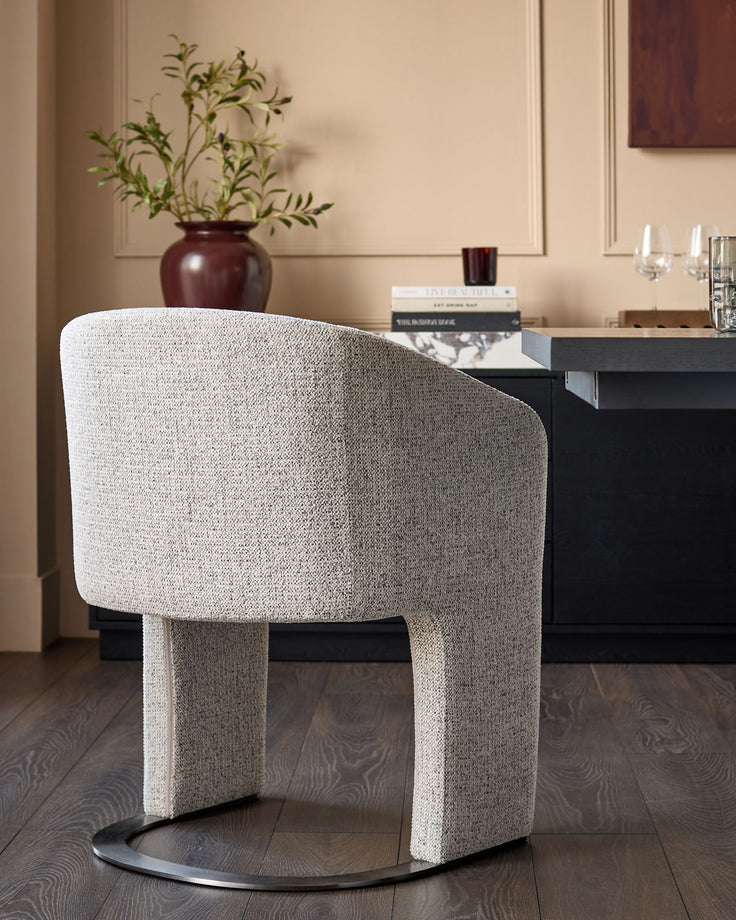 Leighton dining chair in grey chenille fabric with black chrome base, shown from rear angle in styled room setting.
