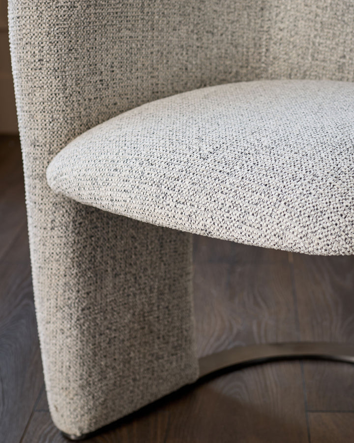 Leighton dining chair in grey chenille fabric, curved design, detail view of seat and backrest on dark wood floor.