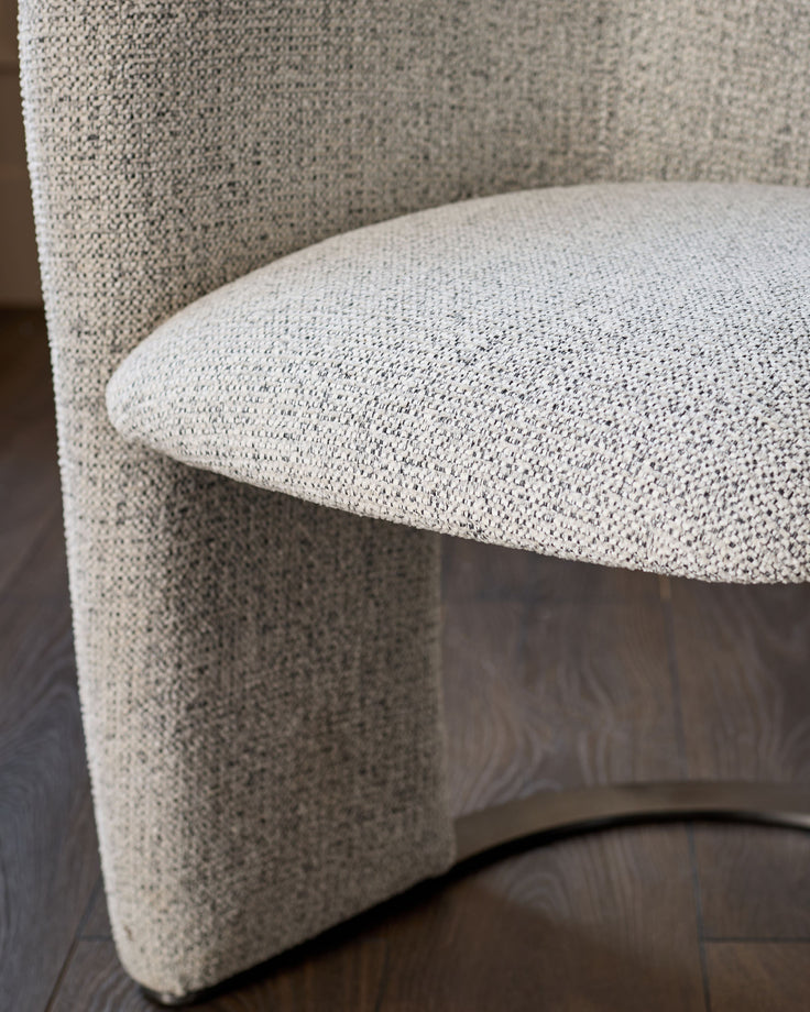 Leighton dining chair in grey chenille fabric, curved design, detail view of seat and backrest on dark wood floor.
