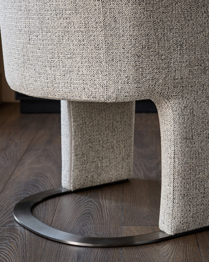 Leighton dining chair in grey chenille fabric with black chrome curved base, shown from low angle detail view.