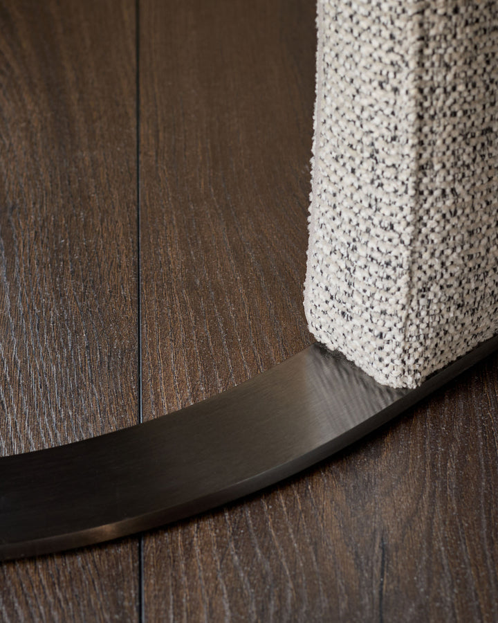 Leighton dining chair base detail showing black chrome curved leg against wood flooring and grey chenille fabric seat.