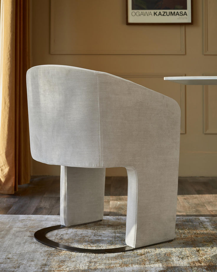 Upholstered dining chair with rounded back and curved metal base, part of a table and rug also visible.