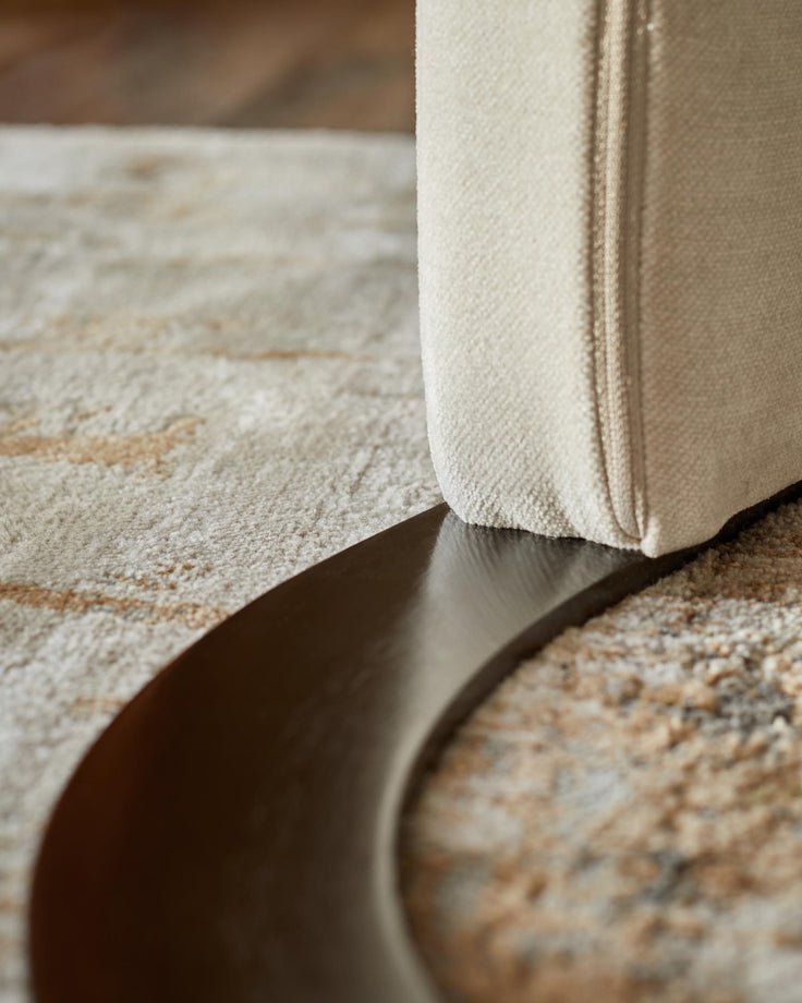Close-up of cream-coloured upholstered furniture with a dark wooden base, placed on a patterned neutral carpet.