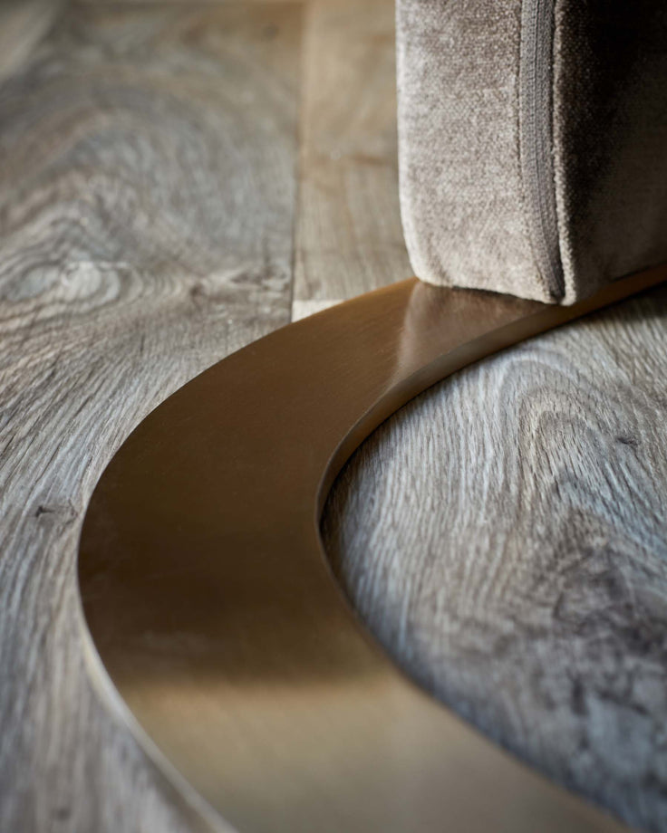 Close-up of a beige chair with a curved, brown metal base on a wood-look floor. Sleek and modern design.