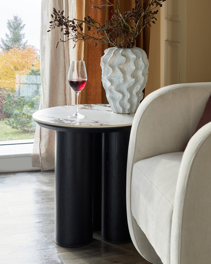 A stylish side table with a marble top, paired with a curvy, neutral-toned armchair.