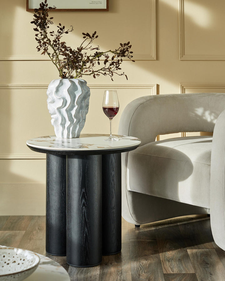 Stylish side table with marble top and dark wood legs, paired with a glass of red wine and a modern grey armchair.