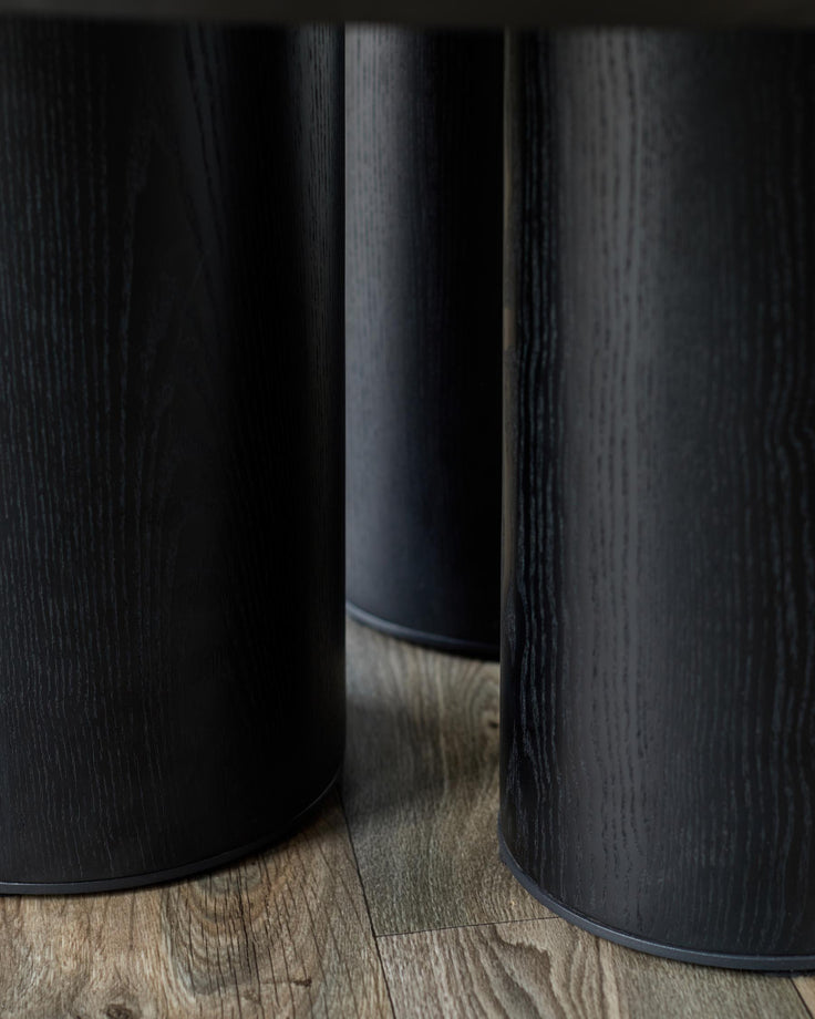 Three black, cylindrical table legs with a wood-grain effect, sat on a wooden floor.