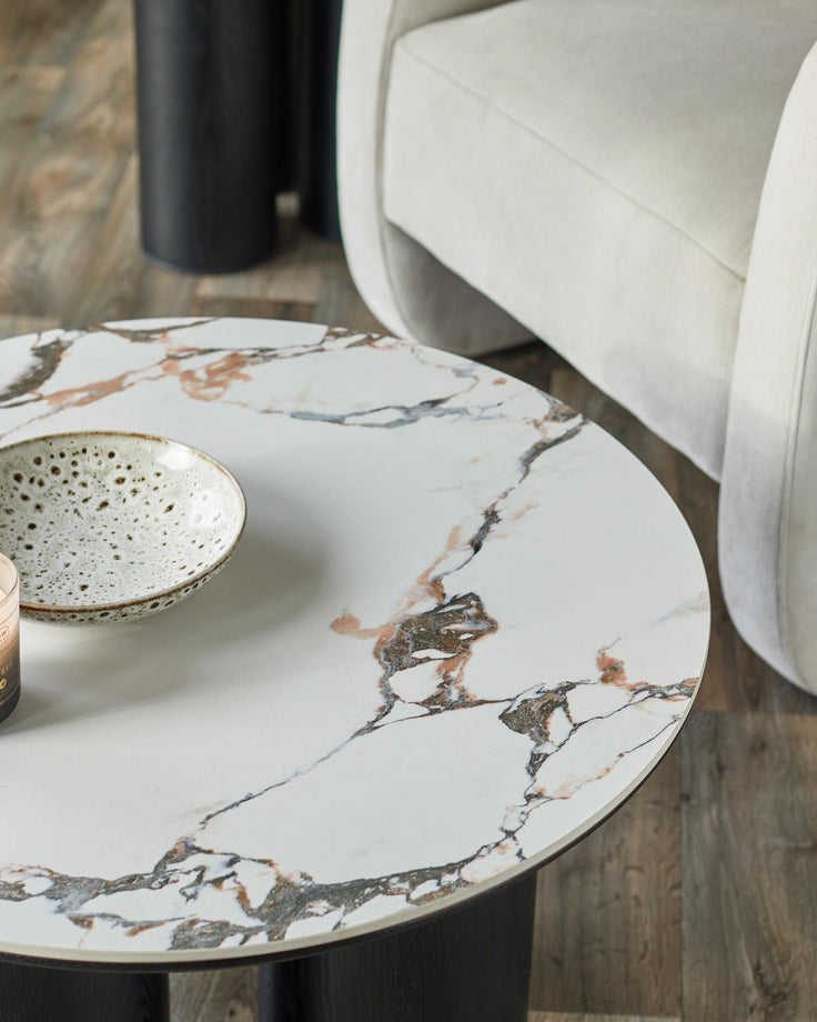 Stylish furniture including a marble-topped coffee table, black side table, and a comfy cream armchair.