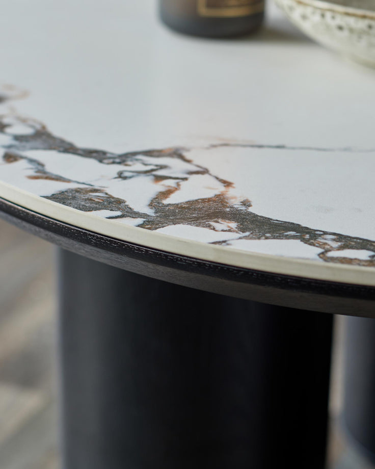 Close-up of a modern, round table with a marble-effect top and dark wooden base. Focus on the texture and design.