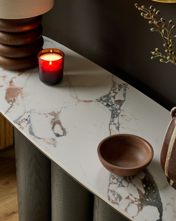 Lena console table in Calacatta white marble with wood base, styled with a red candle and wooden bowl.