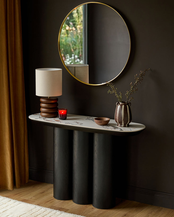 Lena console table in Calacatta white with black cylindrical base, styled with lamp, mirror, and decorative accessories.