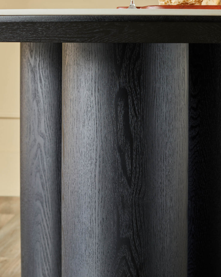 Close-up of a dark wooden table with cylindrical legs, showcasing the wood grain detail and modern design.