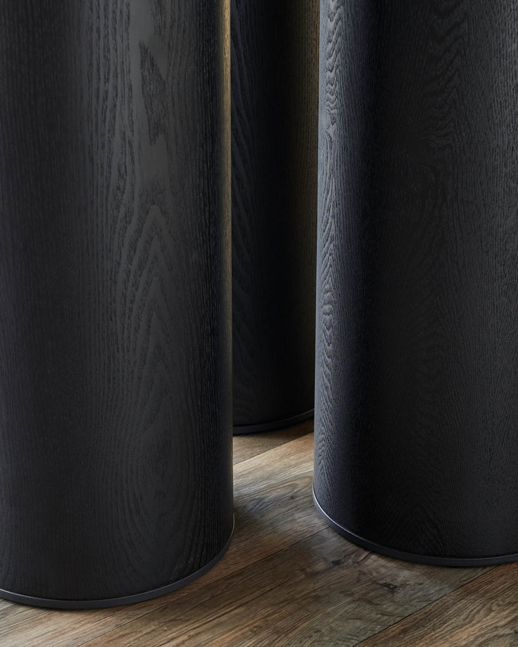 Three dark wood tables with a cylindrical design and a dark wood grain finish on a wooden floor.