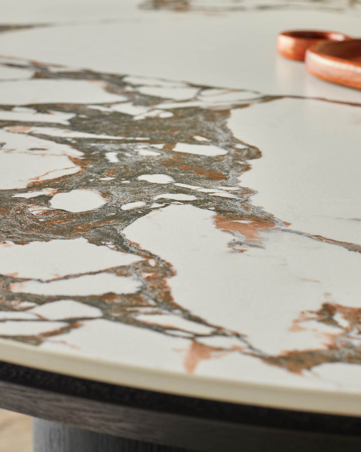 Close-up of a round marble table top with brown and grey veining, supported by a dark wooden base, alongside wooden objects.