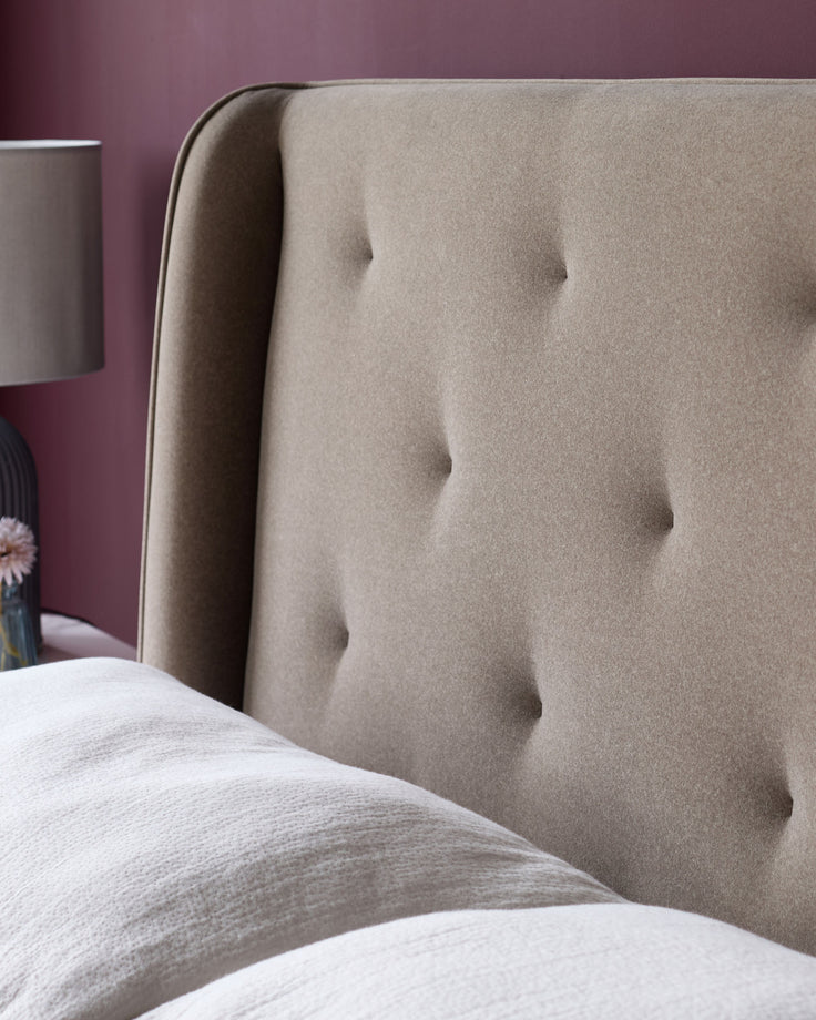 Upholstered headboard with button detailing, complemented by soft bedding and a bedside lamp.