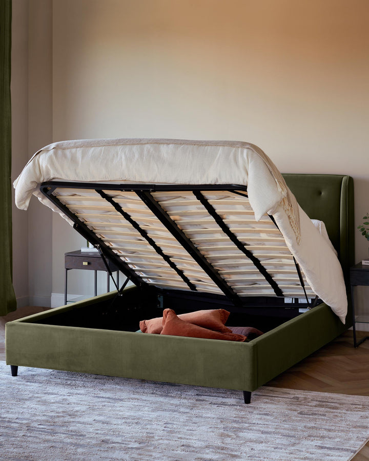 An olive-green ottoman bed, open to reveal storage space, featuring a cream-coloured throw.